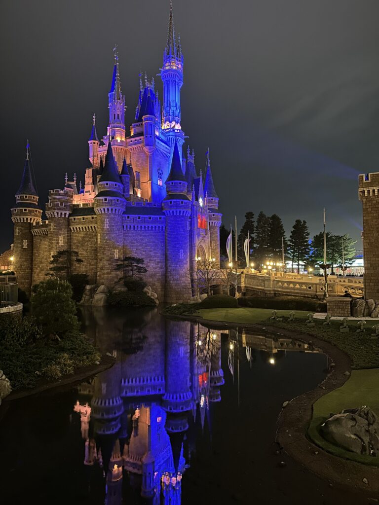 夜の東京ディズニーランドで青や紫色にライトアップされたシンデレラ城と水面に映る城の姿